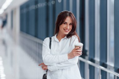 Modern havaalanında ya da gündüz vakti elinde içki bardağıyla beyaz gömlekli esmer bir kadın..