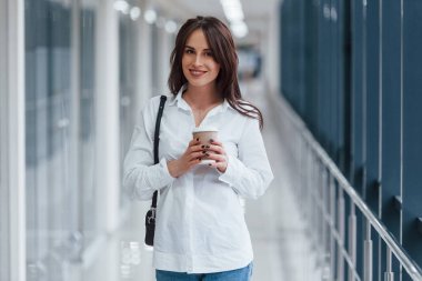 Modern havaalanında ya da gündüz vakti elinde içki bardağıyla beyaz gömlekli esmer bir kadın..