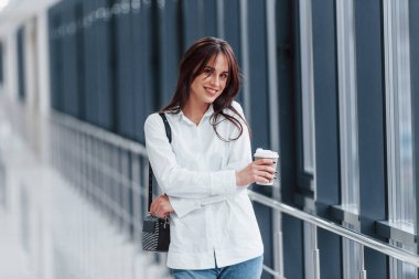 Modern havaalanında ya da gündüz vakti elinde içki bardağıyla beyaz gömlekli esmer bir kadın..