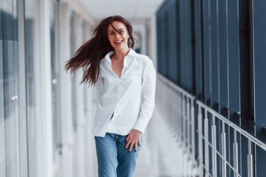 Beyaz gömlekli esmer, modern havaalanında ya da gündüz vakti koridorda yürüyor..