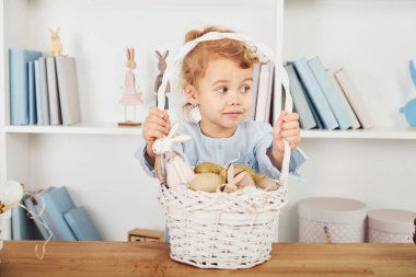 Paskalya tatilini evde, masanın yanında yumurtalı sepetle kutlayan tatlı küçük bir kız..