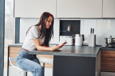 Gündelik giysiler içinde genç, güzel esmer sabah taze içeceklerle mutfakta oturuyor..