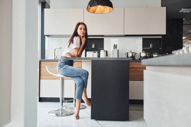 Gündelik giysiler içinde genç, güzel esmer sabah taze içeceklerle mutfakta oturuyor..