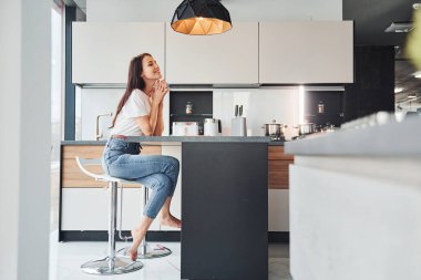 Gündelik giysiler içinde genç, güzel esmer sabah taze içeceklerle mutfakta oturuyor..