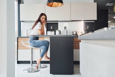 Gündelik giysiler içinde genç, güzel esmer sabah taze içeceklerle mutfakta oturuyor..