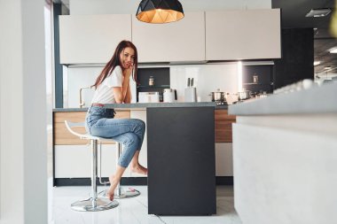 Gündelik giysiler içinde genç, güzel esmer sabah taze içeceklerle mutfakta oturuyor..