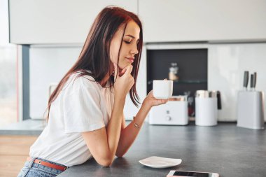 Gündelik giysiler içinde genç, güzel esmer sabah taze içeceklerle mutfakta oturuyor..