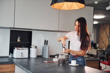 Gündüz vakti mutfakta kahve hazırlayan günlük kıyafetlerle güzel bir esmer kız..