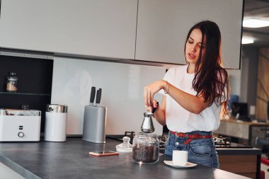 Gündüz vakti mutfakta kahve hazırlayan günlük kıyafetlerle güzel bir esmer kız..