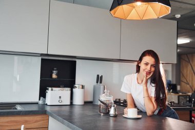 Bir fincan taze kahveyle. Genç ve güzel esmer, gündüzleri evde, mutfakta günlük giysiler içinde..