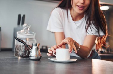 Bir fincan taze kahveyle. Genç ve güzel esmer, gündüzleri evde, mutfakta günlük giysiler içinde..