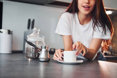 Bir fincan taze kahveyle. Genç ve güzel esmer, gündüzleri evde, mutfakta günlük giysiler içinde..