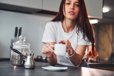 Bir fincan taze kahveyle. Genç ve güzel esmer, gündüzleri evde, mutfakta günlük giysiler içinde..