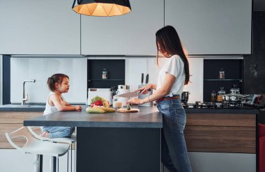 Side view of mother that with her little daughter preparing food indoors in kitchen.