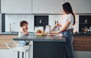 Side view of mother that with her little daughter preparing food indoors in kitchen.