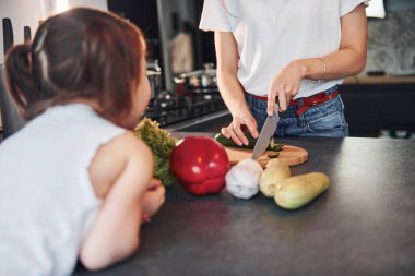 Close up view of mother with her little daughter that preparing food indoors in kitchen.