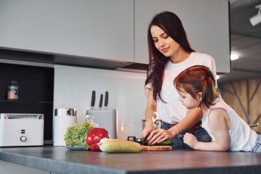 Mother with her little daughter slicing vegetables indoors in kitchen.