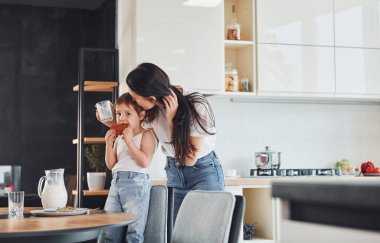 Little girl eats cookies. Mother with her little daughter indoors in kitchen.