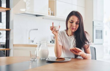 Genç ve güzel esmer, gündüz kıyafetleri içinde, mutfakta bir bardak süt ve şekerle..