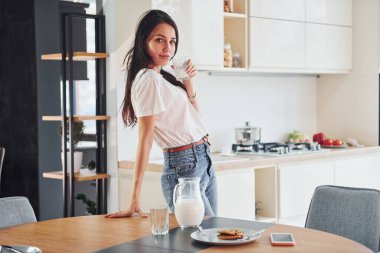 Genç, güzel esmer, günlük giysiler içinde mutfakta, masanın yanında, süt ve kurabiyelerle..