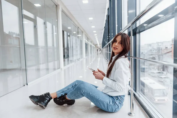 Brunette White Shirt Phone Hands Sits Indoors Modern Airport Hallway —  Fotos de Stock