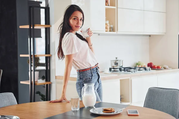 Genç, güzel esmer, günlük giysiler içinde mutfakta, masanın yanında, süt ve kurabiyelerle..