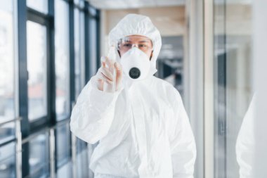Laboratuvar önlüklü, koruyucu gözlüklü ve maskeli kadın doktor içeride antibakteriyel spreyle duruyor..