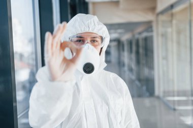 Her şey yoluna girecek, jest yap. Laboratuvar önlüklü, koruyucu gözlüklü ve maskeli kadın doktor içeride dikiliyor..