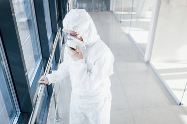 Laboratuvar önlüklü, koruyucu gözlüklü ve maskeli kadın doktor içeride dikiliyor..
