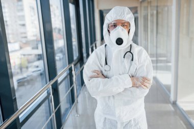 Laboratuvar önlüklü, koruyucu gözlüklü ve maskeli kadın doktor içeride dikiliyor..