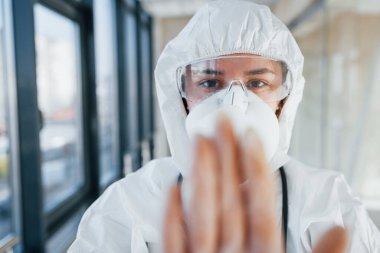 Virüs hareketini durdur. Laboratuvar önlüklü, koruyucu gözlüklü ve maskeli kadın doktor içeride dikiliyor..