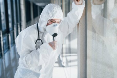 Feels bad and sick. Female doctor scientist in lab coat, defensive eyewear and mask standing indoors.
