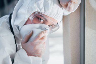 Feels bad and sick. Female doctor scientist in lab coat, defensive eyewear and mask standing indoors.