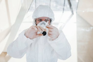 Şırınganın içinde ilaç var. Laboratuvar önlüklü, koruyucu gözlüklü ve maskeli kadın doktor içeride dikiliyor..