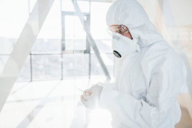 Şırınganın içinde ilaç var. Laboratuvar önlüklü, koruyucu gözlüklü ve maskeli kadın doktor içeride dikiliyor..