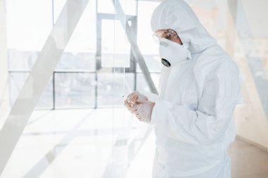 Şırınganın içinde ilaç var. Laboratuvar önlüklü, koruyucu gözlüklü ve maskeli kadın doktor içeride dikiliyor..