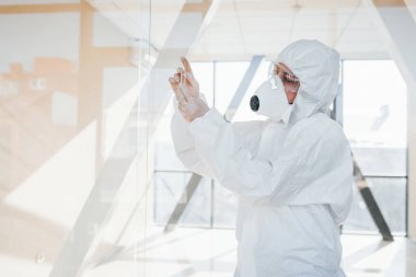 Elinde test tüpüyle. Laboratuvar önlüklü, koruyucu gözlüklü ve maskeli kadın doktor içeride dikiliyor..