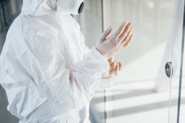 Female doctor scientist in lab coat, defensive eyewear and mask standing indoors and wearing gloves.