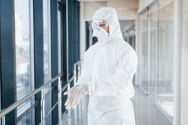 Female doctor scientist in lab coat, defensive eyewear and mask standing indoors and wearing gloves.