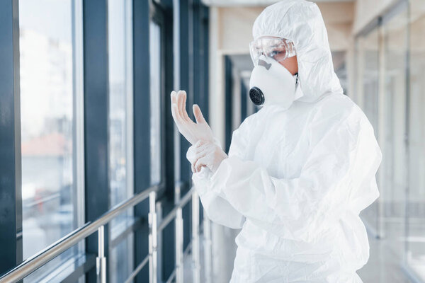Female doctor scientist in lab coat, defensive eyewear and mask standing indoors and wearing gloves.