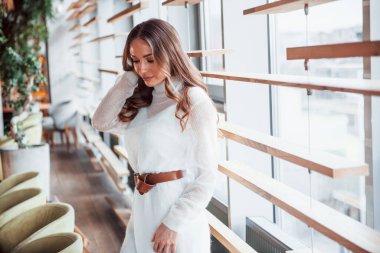 Pencerelerin yanında beyaz elbiseli muhteşem bir kadın duruyor..