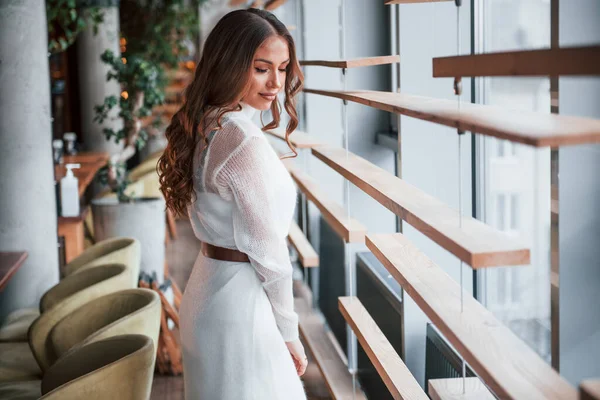 Pencerelerin yanında beyaz elbiseli muhteşem bir kadın duruyor..