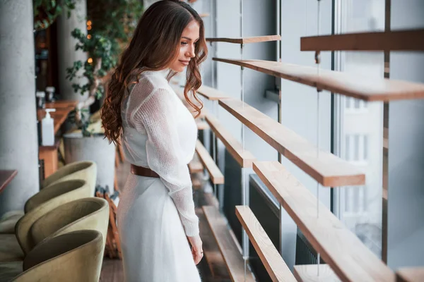 Pencerelerin yanında beyaz elbiseli muhteşem bir kadın duruyor..