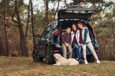 Happy family have fun with their dog near modern car outdoors in forest.