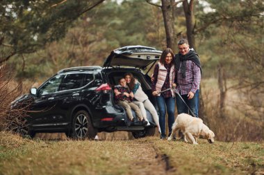Mutlu aile, köpekleriyle ormanda, modern arabanın yanında eğleniyor..