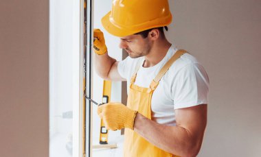 Handyman in yellow uniform installs new window. House renovation conception.