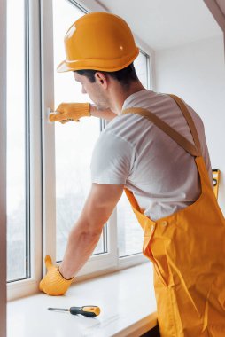 Sarı üniformalı tamirci yeni pencere takıyor. Ev yenileme konsepti.