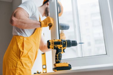 Sarı üniformalı tamirci otomatik tornavida kullanarak yeni pencere kuruyor. Ev yenileme konsepti.