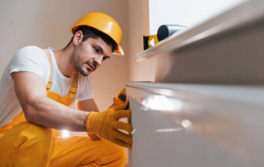 Handyman in yellow uniform installing new battery. House renovation conception.