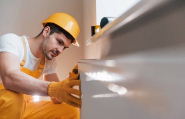 Handyman in yellow uniform installing new battery. House renovation conception.